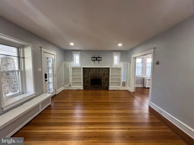 a view of an empty room with wooden floor fireplace and a window