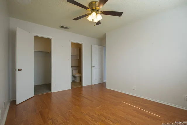 an empty room with wooden floor chandelier fan and windows