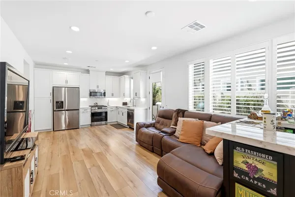 a living room with stainless steel appliances furniture a rug kitchen view and a large window