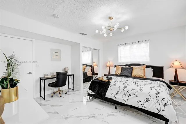 a bedroom with a bed a chair and potted plant on the dresser