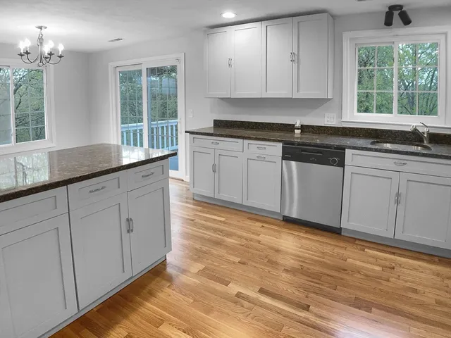 a kitchen with granite countertop white cabinets white appliances wooden floor and a window