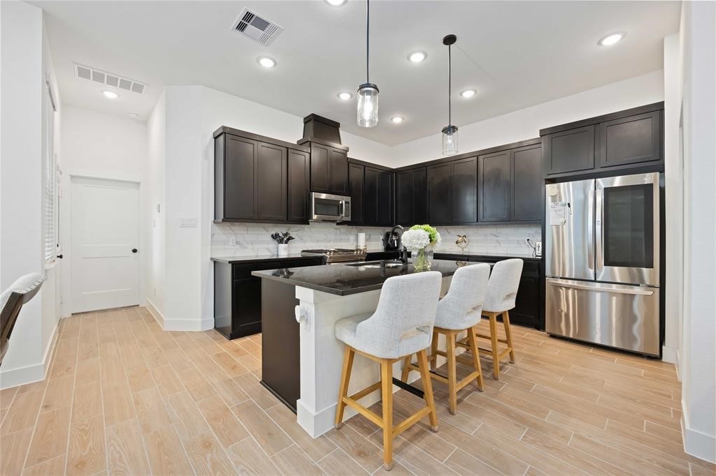 10014 Nectar Path Iowa Colony, TX 77583 - Photo 8 of 26 This modern kitchen features sleek dark cabinetry, stainless steel appliances, and a spacious island with seating for four. The light wood flooring and recessed lighting create a bright, inviting space ideal for cooking and entertaining.
