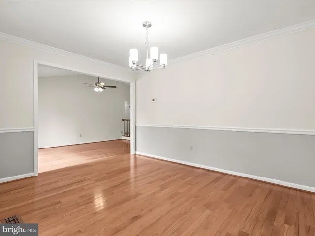 an empty room with wooden floor chandelier and windows