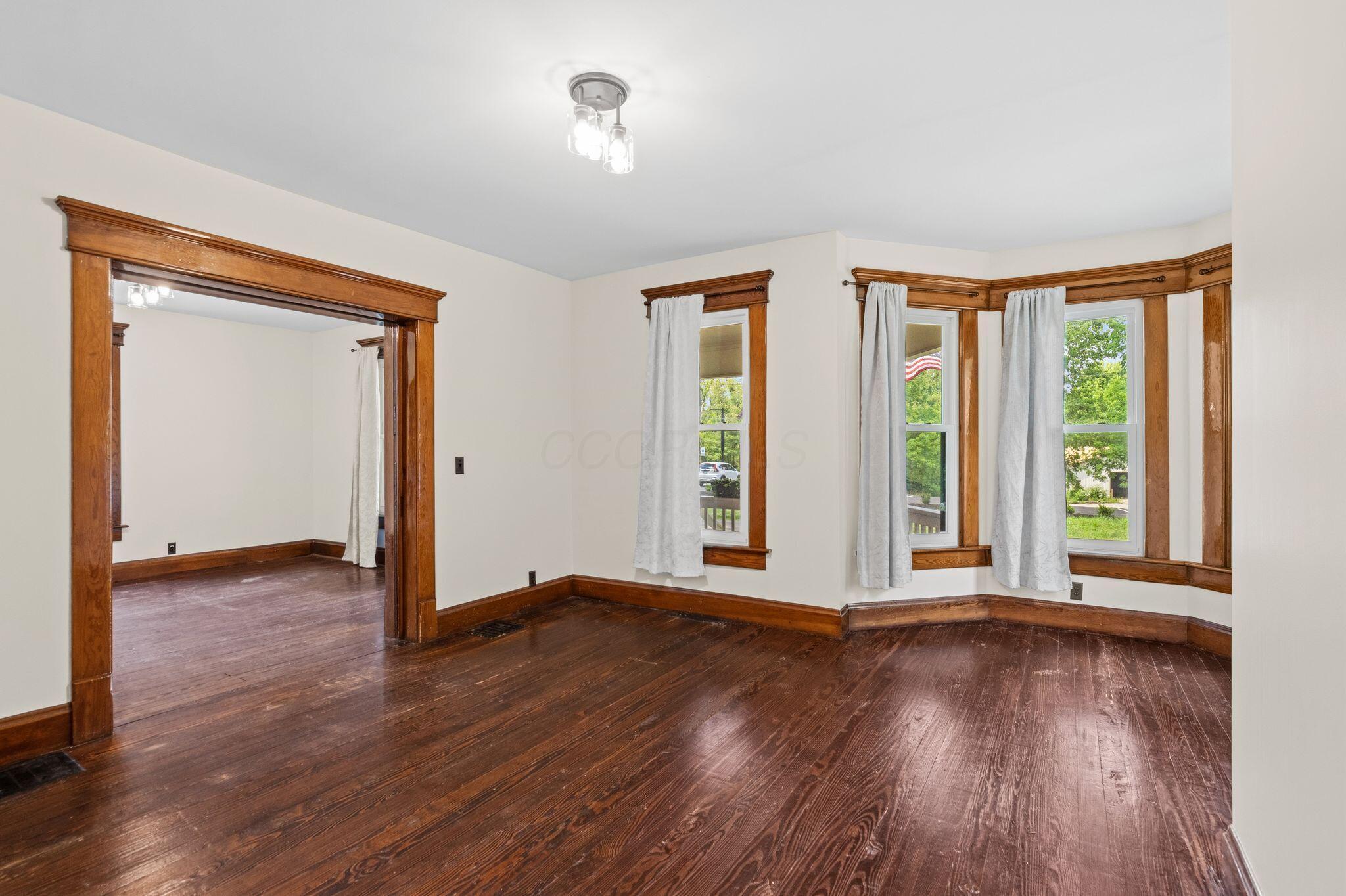 107 Price Road Columbus, OH 43230 - Photo 6 of 51 Bay window with natural light, rich wood-finish flooring, white walls, wood trim, and a three-light flush-mount ceiling fixture