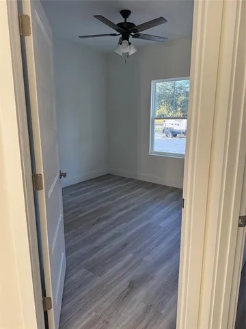 an empty room with wooden floor fan and windows