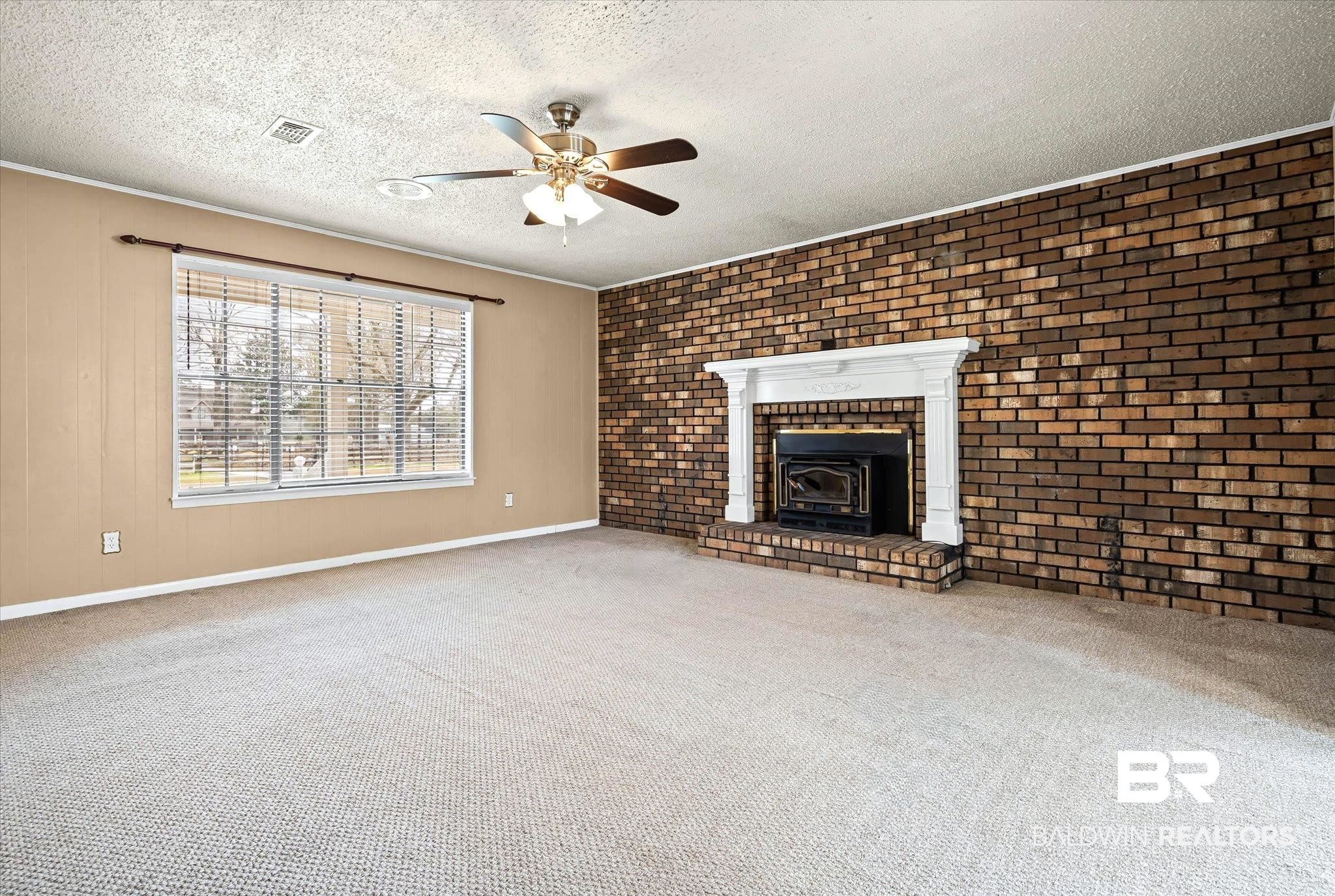 8090 Murray Hill Road Irvington, AL 36544 - Photo 9 of 40 Unfurnished living room featuring brick wall, carpet flooring, a ceiling fan, a textured ceiling, and a fireplace with insert