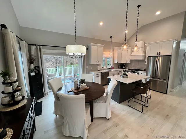 a kitchen with stainless steel appliances granite countertop a refrigerator a sink dishwasher a dining table and chairs with the wooden floor