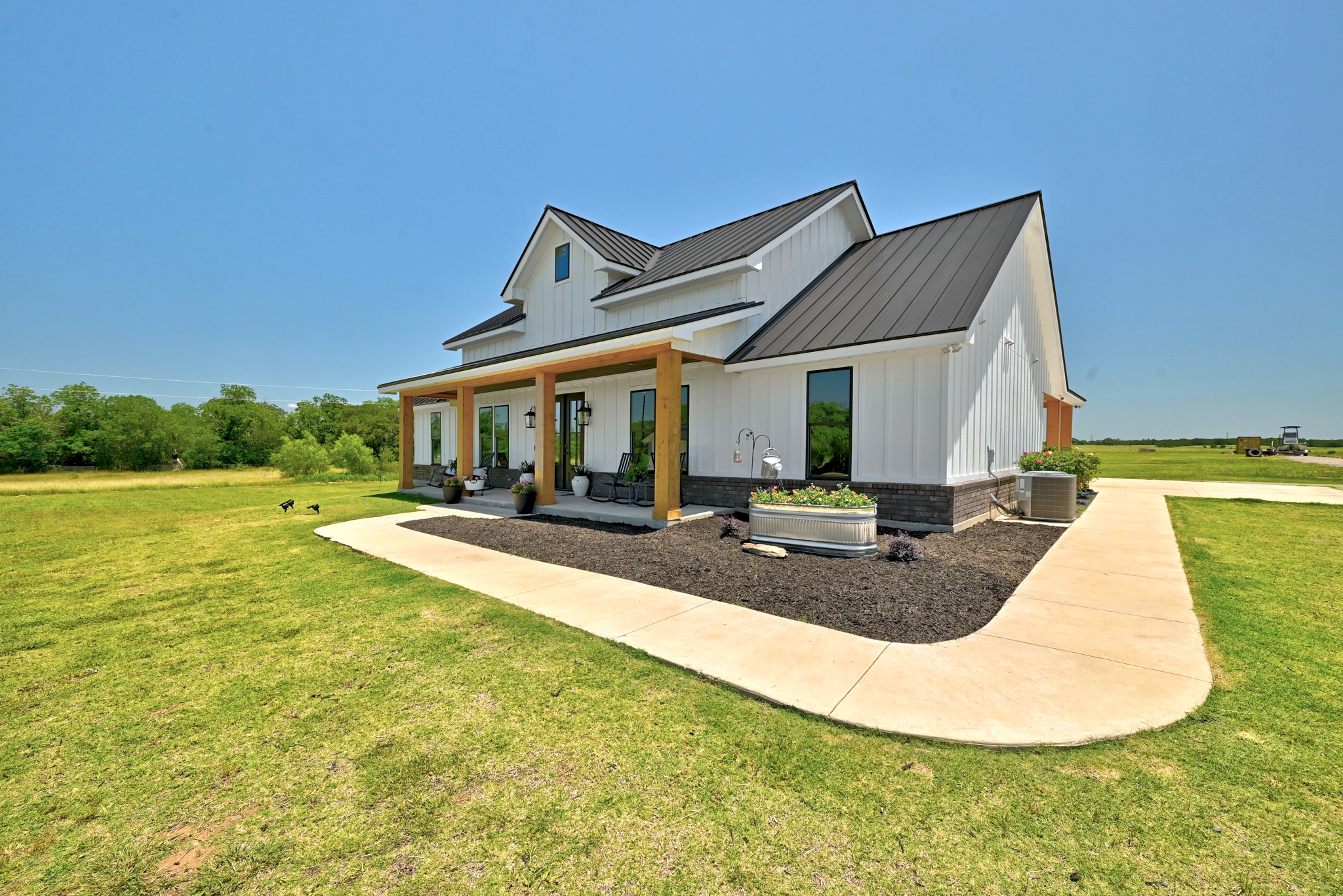 2889 Old McMahan Road Lockhart, TX 78644 - Photo 6 of 33 White siding and a dark roof define this inviting farmhouse, set against a verdant, expansive landscape.