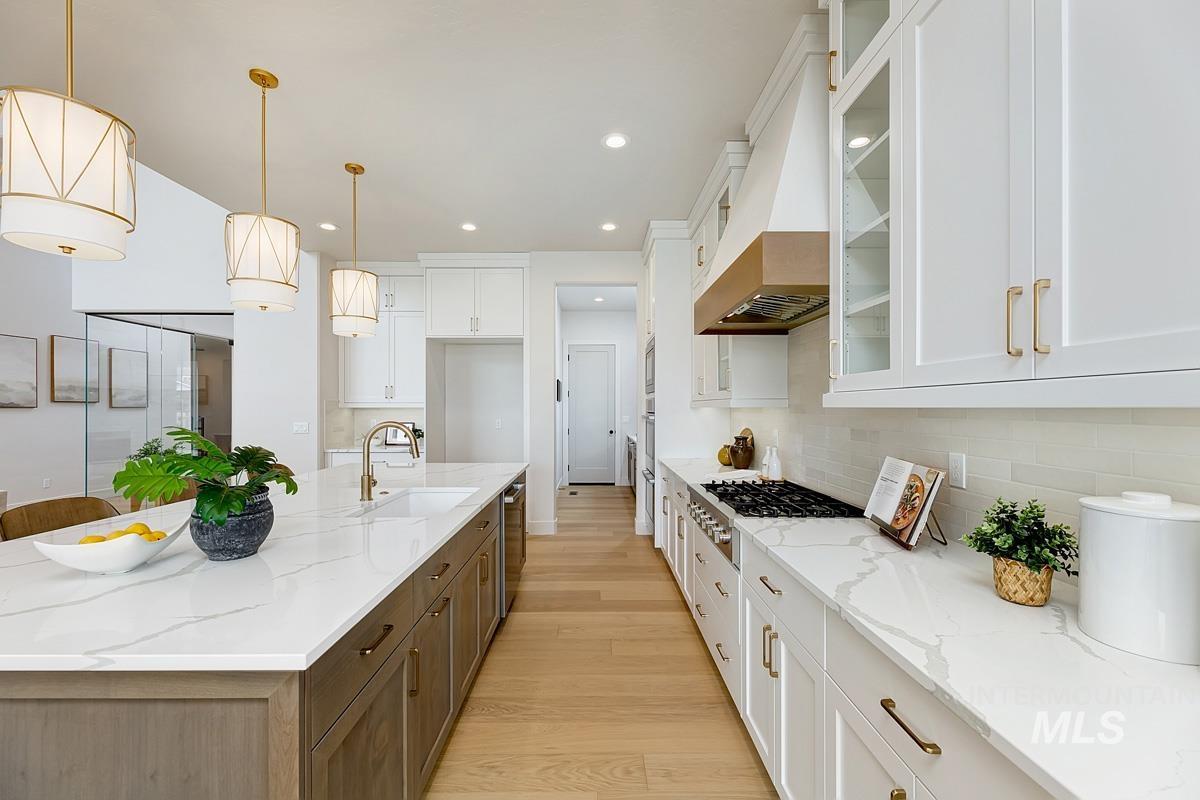 7026 Saddle Bred Way Star, ID 83669 - Photo 12 of 49 Kitchen with two tone cabinetry, glass insert cabinets, light stone countertops, light wood-style floors, and hanging light fixtures