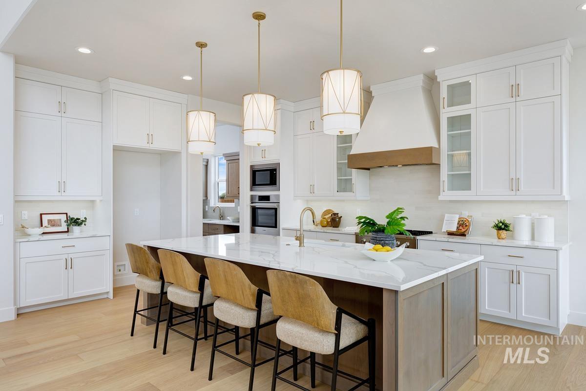 7026 Saddle Bred Way Star, ID 83669 - Photo 4 of 49 Two tone kitchen featuring decorative light fixtures, a breakfast bar area, light stone countertops, light wood finished floors, and an island with sink