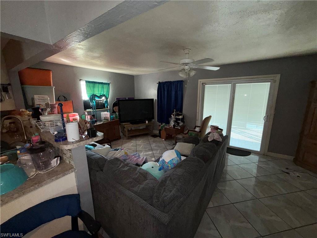 117 Robert Avenue Lehigh Acres, FL 33936 - Photo 5 of 20 Living area with a textured ceiling, light tile patterned floors, ceiling fan, and healthy amount of natural light