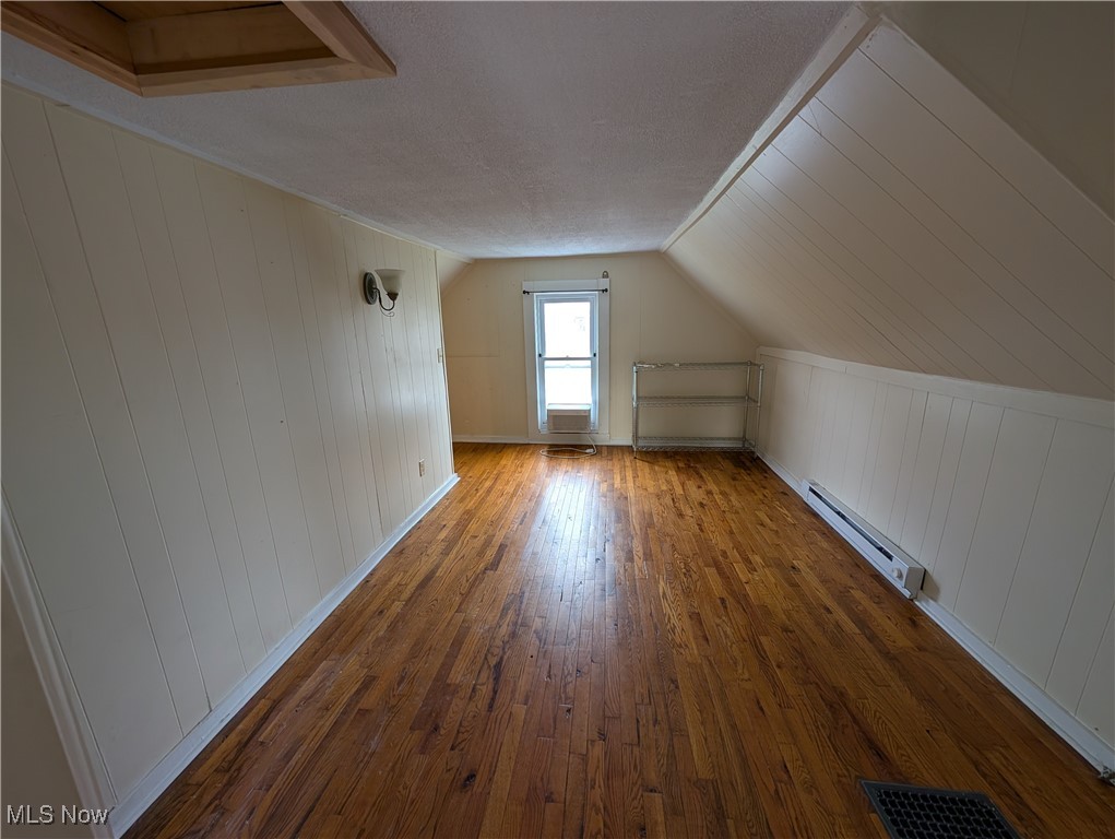 10143 Pleasant Road Pleasant City, OH 43772 - Photo 22 of 32 Bonus room featuring wood-type flooring, baseboard heating, wooden walls, a textured ceiling, and lofted ceiling