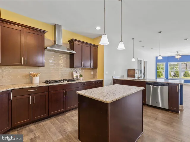 a kitchen with kitchen island granite countertop wooden cabinets a refrigerator a sink a stove and a wooden floors