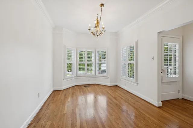 an empty room with wooden floor chandelier and windows