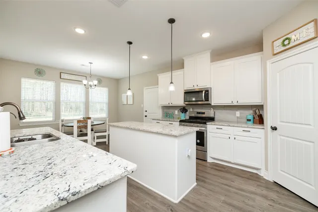 a kitchen with stainless steel appliances kitchen island granite countertop a sink a stove a refrigerator and white cabinets with wooden floor