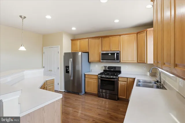 a kitchen with stainless steel appliances granite countertop a refrigerator a sink dishwasher a stove and white countertops with wooden floor