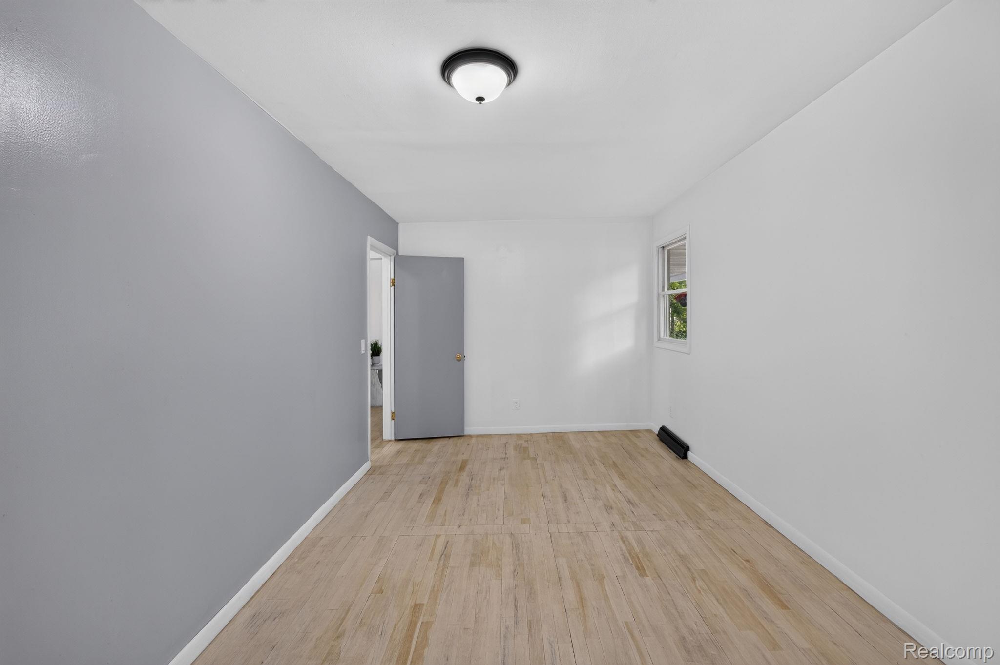 9288 Hilda Lane Flushing, MI 48433 - Photo 19 of 50 Open room featuring wood-finish flooring, a neutral color palette with one accent wall, white baseboards, and a semi-flush ceiling light fixture