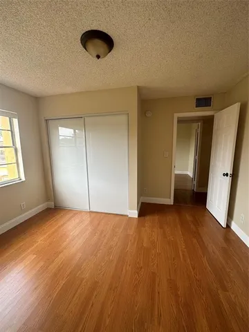 a view of an empty room with wooden floor and closet