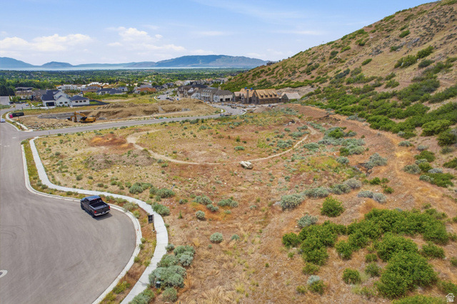 1817 North Dean Court, Unit 12 Alpine, UT 84004 - Photo 23 of 38 Expansive undeveloped lot featuring natural vegetation, a curved paved road, and a concrete sidewalk