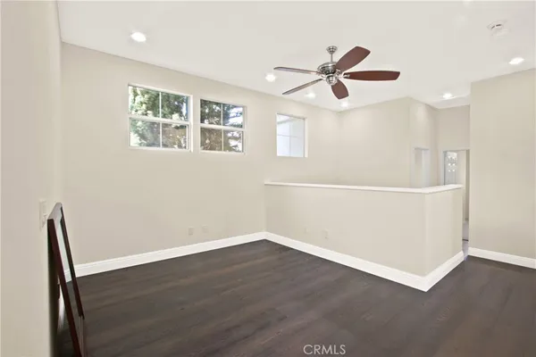 a view of an empty room with wooden floor and a ceiling fan