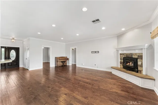 an empty room with wooden floor fire place and kitchen view