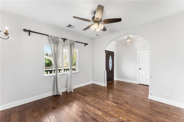 a view of an empty room with wooden floor and a ceiling fan