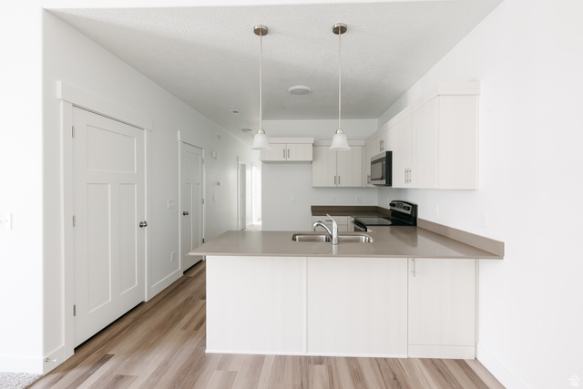 4653 South Alder Drive, Unit H304 Mapleton, UT 84664 - Photo 5 of 14 Kitchen with white cabinetry, stainless steel appliances, a peninsula, light wood finished floors, and hanging light fixtures
