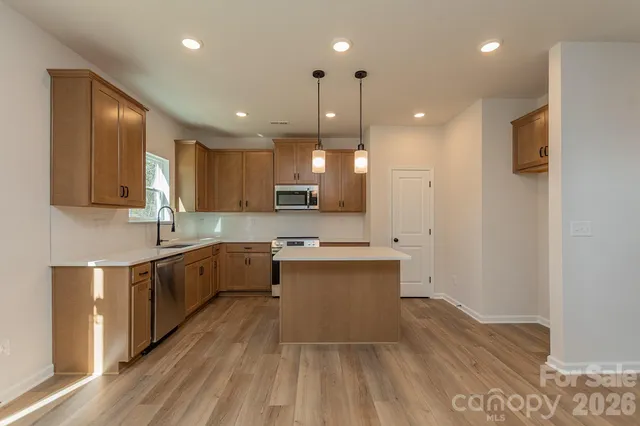 a large kitchen with stainless steel appliances a large counter top a sink dishwasher a refrigerator and white cabinets next to a window