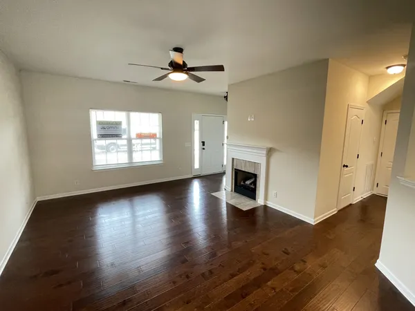 an empty room with wooden floor a ceiling fan a fireplace and windows