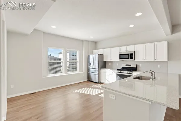 a kitchen with stainless steel appliances a stove top oven a sink a refrigerator a white cabinets and wooden floor