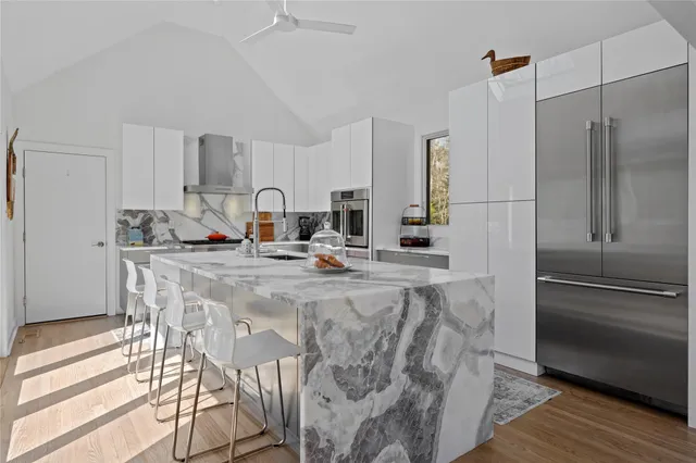 a kitchen with stainless steel appliances kitchen island granite countertop a refrigerator a stove and white cabinets with wooden floor