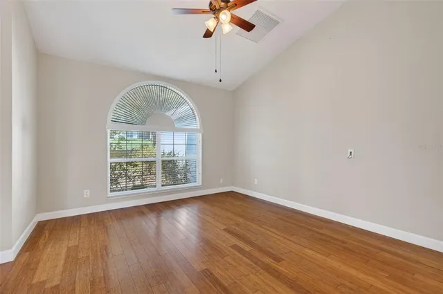 an empty room with wooden floor chandelier fan and windows