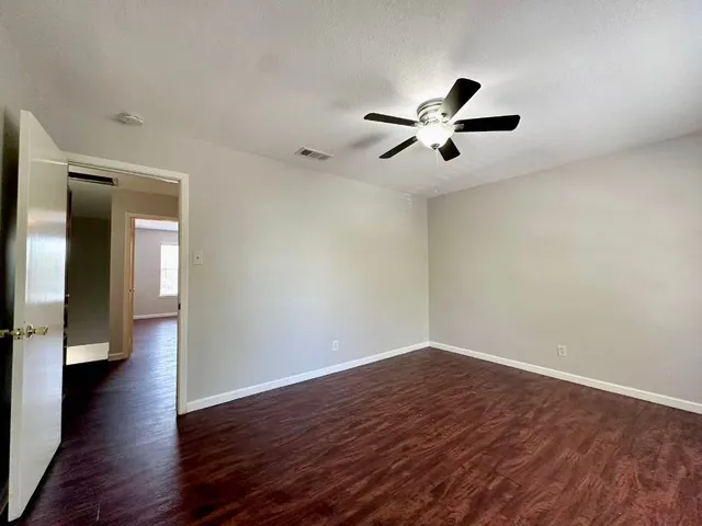 an empty room with wooden floor and a ceiling fan