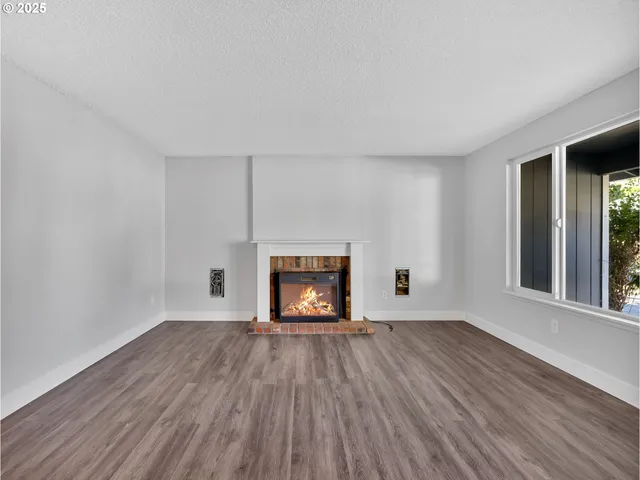 a view of an empty room with wooden floor fire place and a window