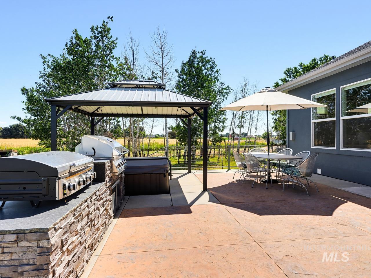 4950 West Columbia Road Nampa, ID 83687 - Photo 42 of 50 Expansive stamped concrete patio featuring an outdoor kitchen with a stone facade, a dedicated grilling area, and a metal gazebo
