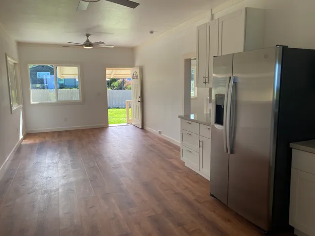 a view of an empty room with wooden floor and a kitchen
