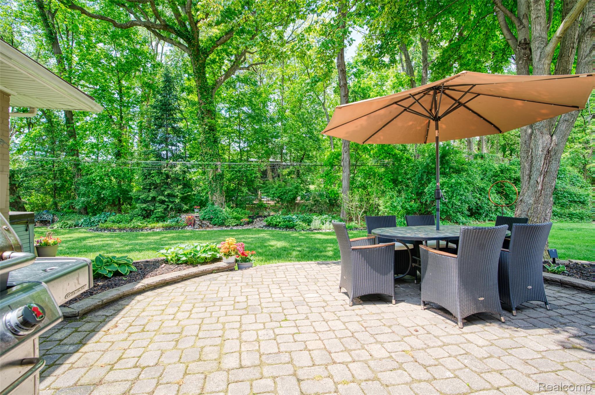 2172 Devonshire Road Bloomfield Hills, MI 48302 - Photo 36 of 45 Paved patio area featuring light-colored pavers, a built-in garden bed with dark mulch, and a lush green lawn
