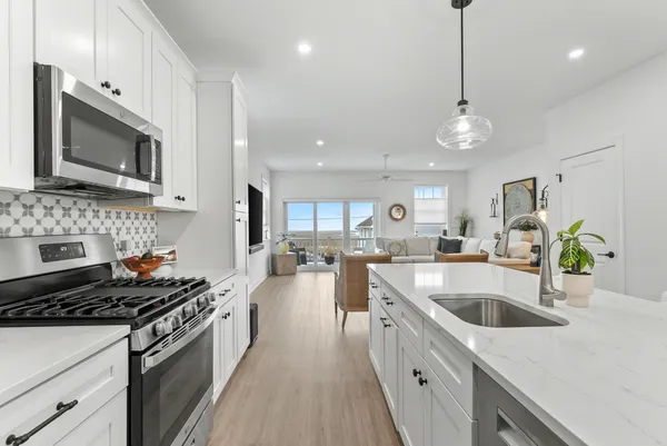 a large white kitchen with stainless steel appliances kitchen island a stove a sink a refrigerator and a dining table with wooden floor