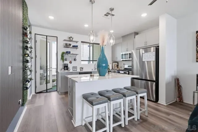 a kitchen with stainless steel appliances kitchen island granite countertop a refrigerator a stove a sink a dining table and chairs with wooden floor