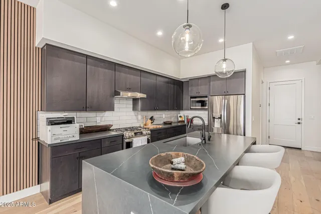 a kitchen with stainless steel appliances kitchen island granite countertop a sink a stove a refrigerator and chairs