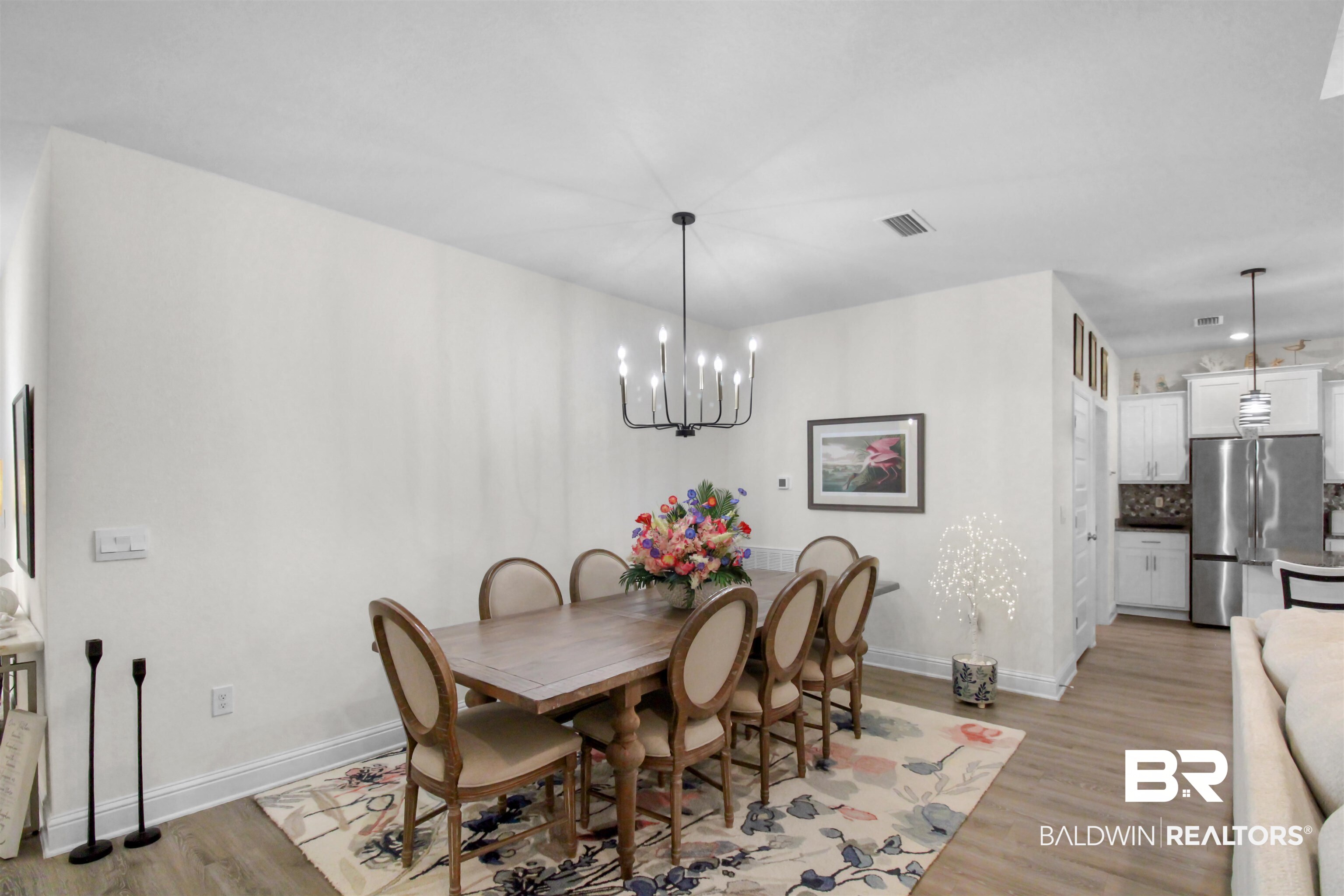 1885 Carly Street Foley, AL 36535 - Photo 15 of 40 Open-concept living space featuring wood-finish flooring, a contemporary chandelier, and a kitchen with white cabinetry, a stainless steel refrigerator, and pendant lighting