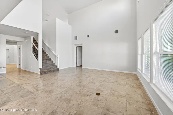 an empty room with a chandelier fan and kitchen view