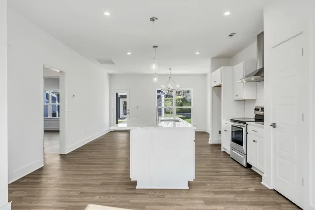 a large kitchen with stainless steel appliances granite countertop a large center island a stove a refrigerator white cabinets and wooden floor