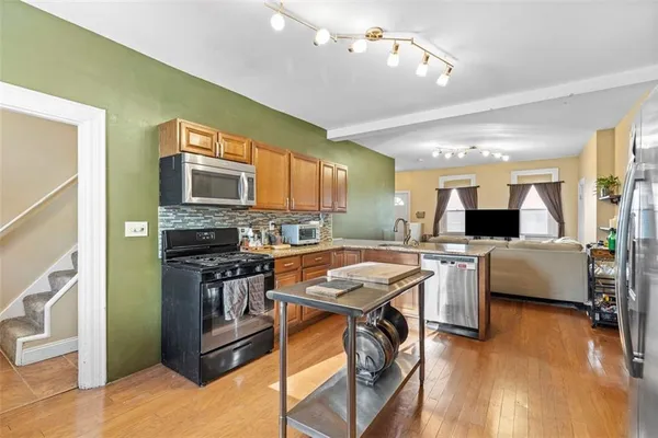 a kitchen with stainless steel appliances granite countertop a stove top oven a sink dishwasher a dining table and chairs with wooden floor