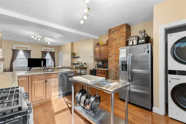 a kitchen with stainless steel appliances kitchen island granite countertop a refrigerator a stove top oven a sink a dining table and chairs with wooden floor