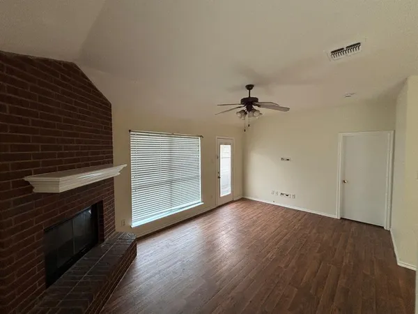a view of an empty room with wooden floor a fireplace and a window