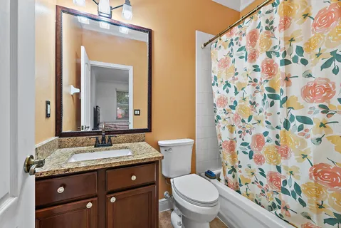 a bathroom with a granite countertop toilet a sink a mirror a shower curtain and a shower curtain