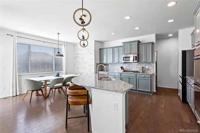 a kitchen with stainless steel appliances kitchen island granite countertop a stove top oven a sink a dining table and chairs with wooden floor