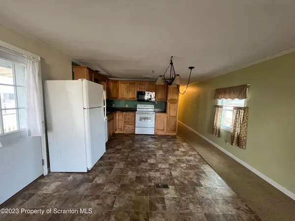 a view of a refrigerator in kitchen and an empty room with wooden floor and a window