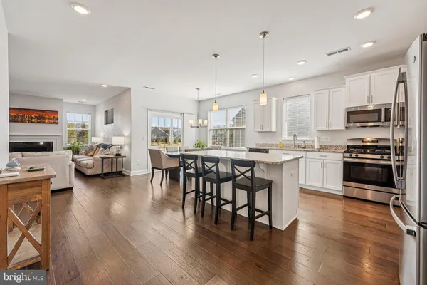 a kitchen with stainless steel appliances kitchen island granite countertop a stove top oven a sink a dining table and chairs with wooden floor